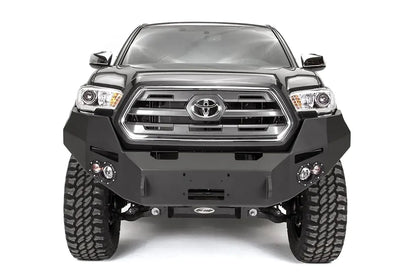 Fab Fours Premium front bumper on a dark gray Toyota Tacoma, straight-on front view, showing the full-width bumper, round fog lights, and winch mount plate