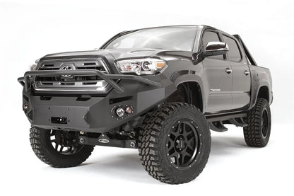 Fab Fours Premium front bumper with pre-runner guard on a dark gray Toyota Tacoma, front three-quarter view, showing the pre-runner hoop, round fog lights, and winch-ready center section