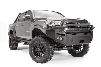 Fab Fours Premium front bumper with pre-runner guard on a dark gray Toyota Tacoma, front three-quarter view, showing the pre-runner hoop, round fog lights, and wraparound end caps