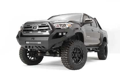 Fab Fours Vengeance front bumper on a dark gray Toyota Tacoma, front three-quarter view, showing the no-guard design, LED light bar, and cube light pods