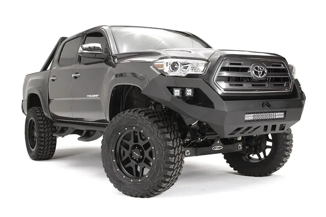 Fab Fours Vengeance front bumper on a dark gray Toyota Tacoma, front three-quarter view, showing the LED light bar, cube light pods, and skid plate