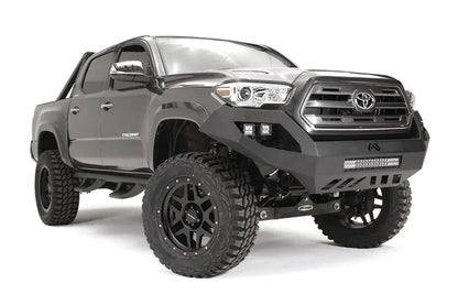 Fab Fours Vengeance front bumper on a dark gray Toyota Tacoma, front three-quarter view, showing the LED light bar, cube light pods, and skid plate