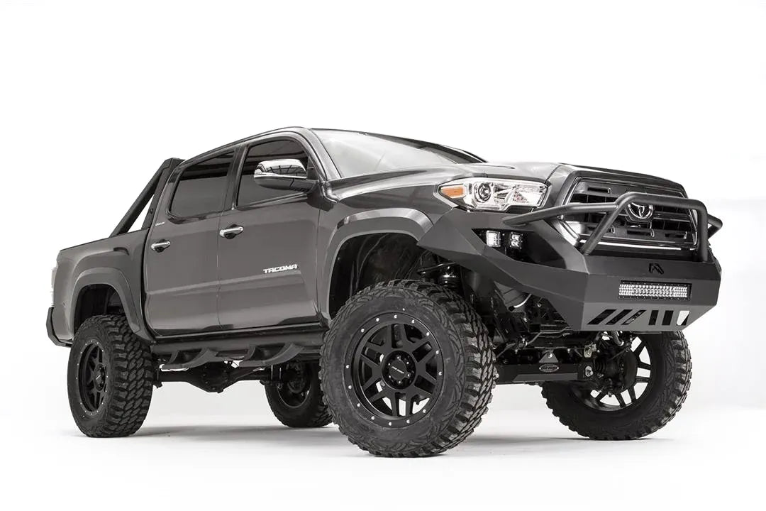 Fab Fours Vengeance front bumper with high pre-runner guard on a dark gray Toyota Tacoma, front three-quarter view, showing the pre-runner hoop, cube light pods, and LED light bar