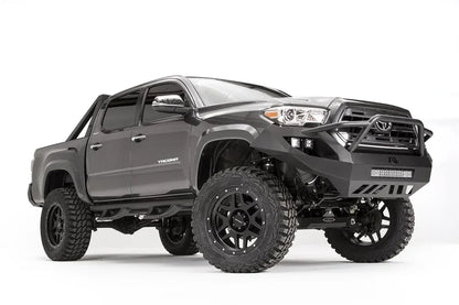 Fab Fours Vengeance front bumper with high pre-runner guard on a dark gray Toyota Tacoma, front three-quarter view, showing the pre-runner hoop, cube light pods, and LED light bar