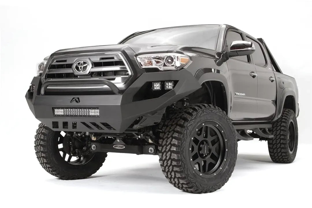 Fab Fours Vengeance front bumper with low pre-runner guard on a dark gray Toyota Tacoma, front three-quarter view, showing the low guard hoop, LED light bar, and cube light pods