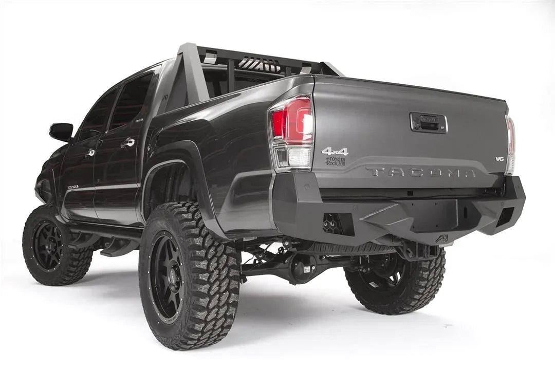Fab Fours Vengeance rear bumper on a dark gray Toyota Tacoma, rear three-quarter view, showing the angular end caps, recessed light pods, and center plate mount