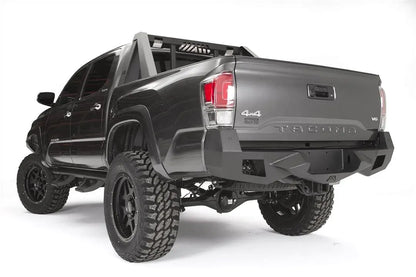 Fab Fours Vengeance rear bumper on a dark gray Toyota Tacoma, rear three-quarter view, showing the angular end caps, recessed light pods, and center plate mount