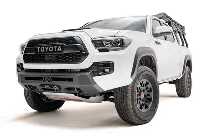 Fab Fours Hidden Winch Mount on a white Toyota Tacoma, front three-quarter view, showing the low-profile winch plate, hidden winch fairlead, and factory-style bumper fit