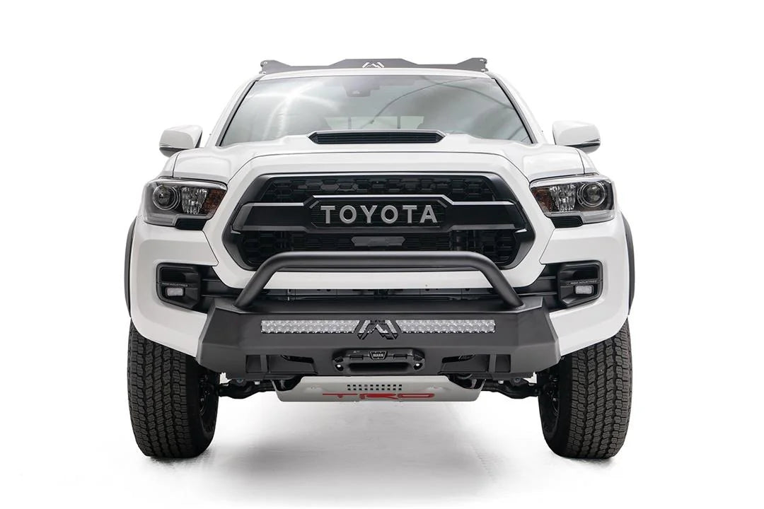 Fab Fours Hidden Winch Mount with low pre-runner guard on a white Toyota Tacoma, straight-on front view, showing the low guard hoop, LED light bar, and center fairlead