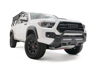 Fab Fours Hidden Winch Mount with low pre-runner guard on a white Toyota Tacoma, front three-quarter view, showing the guard hoop, light bar, and winch plate