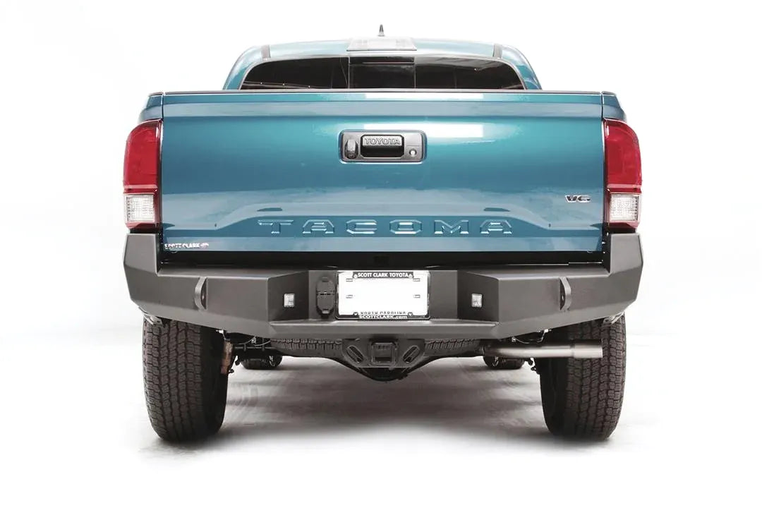 Fab Fours Premium rear bumper on a blue Toyota Tacoma, straight-on rear view, showing the full bumper width, recessed cube lights, and center plate mount