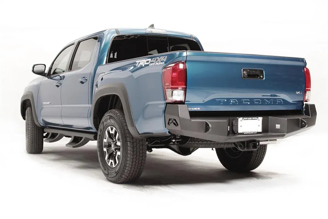 Fab Fours Premium rear bumper on a blue Toyota Tacoma, rear three-quarter view, showing the recessed cube lights, center plate mount, and angled end caps