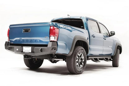 Fab Fours Premium rear bumper on a blue Toyota Tacoma, rear three-quarter view, showing the recessed cube lights, plate mount, and wraparound end cap