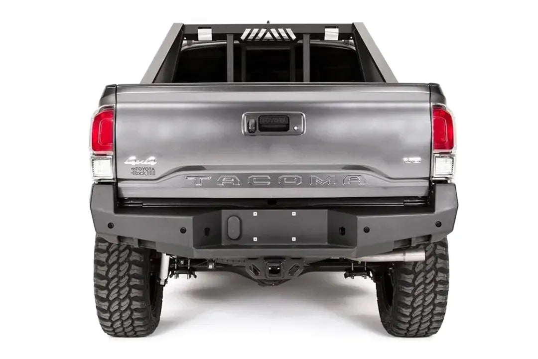 Fab Fours Premium rear bumper on a dark gray Toyota Tacoma, straight-on rear view, showing the full bumper width, center plate mount, and receiver hitch