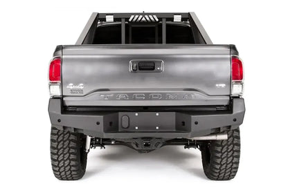 Fab Fours Premium rear bumper on a dark gray Toyota Tacoma, straight-on rear view, showing the full bumper width, center plate mount, and receiver hitch