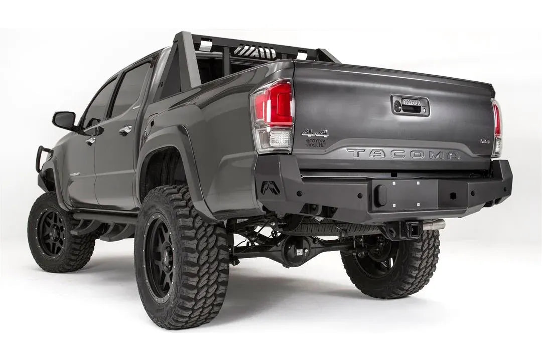Fab Fours Premium rear bumper on a dark gray Toyota Tacoma, rear three-quarter view, showing the angled end cap, plate mount, and receiver hitch