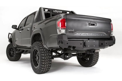 Fab Fours Premium rear bumper on a dark gray Toyota Tacoma, rear three-quarter view, showing the angled end cap, plate mount, and receiver hitch