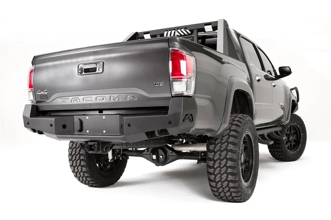 Fab Fours Premium rear bumper on a dark gray Toyota Tacoma, rear three-quarter view, showing the sensor-ready face, angled end caps, and center plate mount