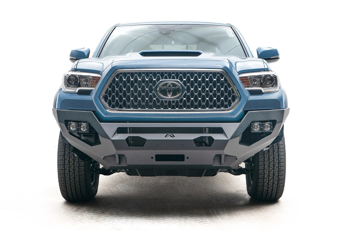 Fab Fours Matrix front bumper on a blue Toyota Tacoma, straight-on front view, showing the no-guard design, cube light pods, and winch mount opening