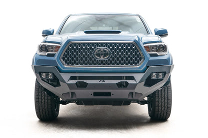 Fab Fours Matrix front bumper on a blue Toyota Tacoma, straight-on front view, showing the no-guard design, cube light pods, and winch mount opening