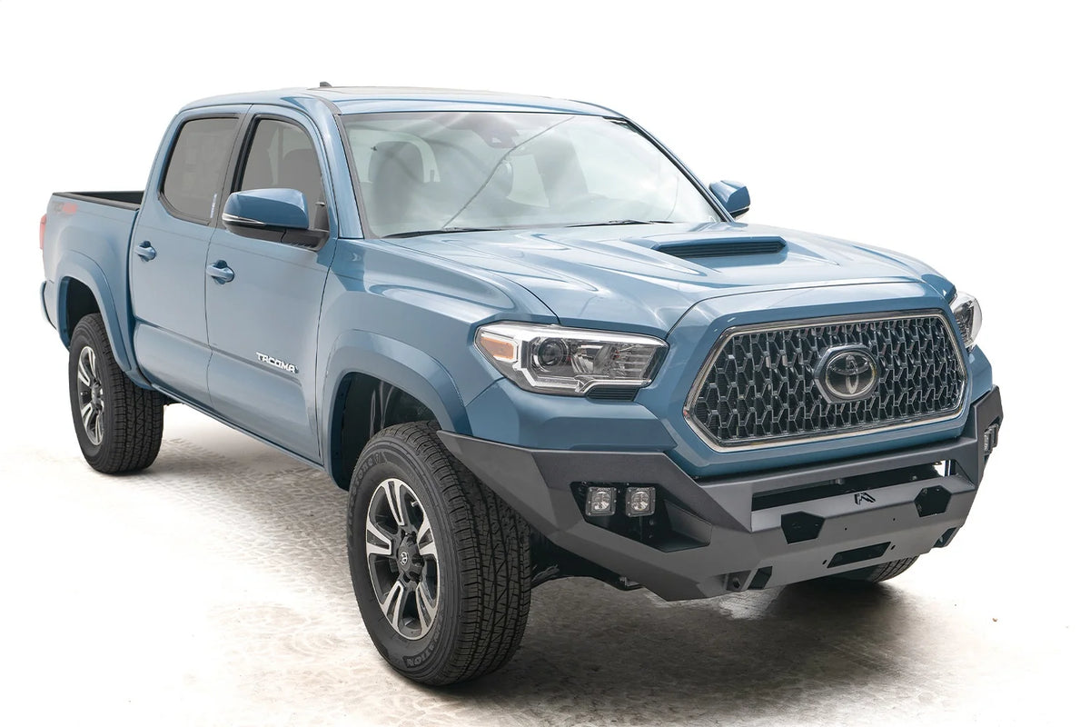 Fab Fours Matrix front bumper on a blue Toyota Tacoma, front three-quarter view, showing the cube light pods, winch opening, and angular end caps