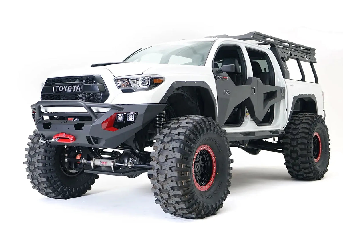 Fab Fours Matrix front bumper with pre-runner guard on a white Toyota Tacoma, front three-quarter view, showing the pre-runner hoop, winch with red hook, and cube light pods