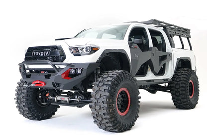 Fab Fours Matrix front bumper with pre-runner guard on a white Toyota Tacoma, front three-quarter view, showing the pre-runner hoop, winch with red hook, and cube light pods