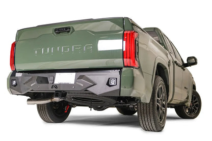 Fab Fours Vengeance rear bumper on a green Toyota Tundra, rear three-quarter view, showing the angular faceted face, cube light pod, and plate mount