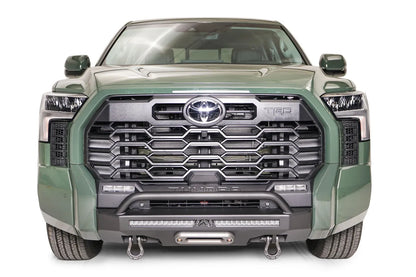 Fab Fours Hidden Winch Mount with pre-runner guard on a green Toyota Tundra, straight-on front view, showing the guard hoop, LED light bar, and D-ring shackles