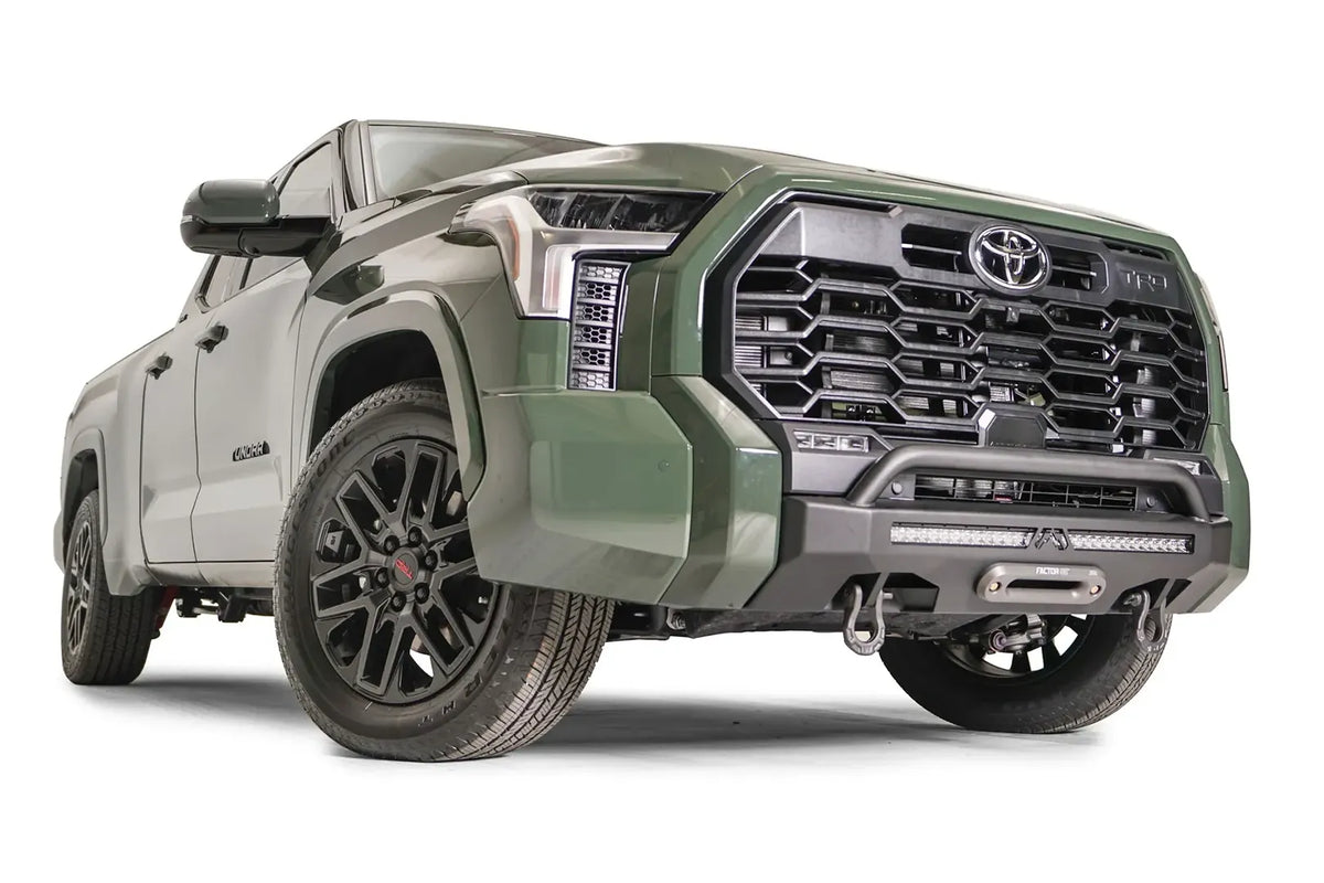 Fab Fours Hidden Winch Mount with pre-runner guard on a green Toyota Tundra, front three-quarter view, showing the low guard hoop, LED light bar, and winch fairlead