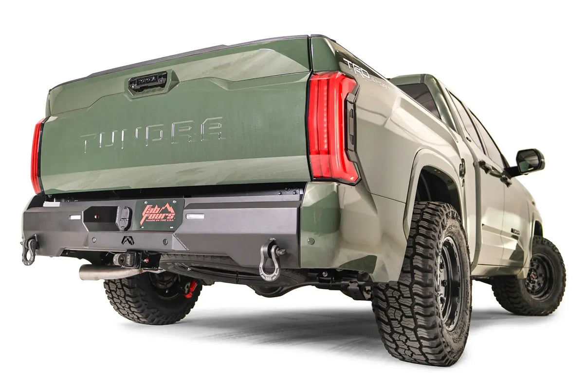 Fab Fours Premium rear bumper on a green Toyota Tundra, rear three-quarter view, showing the recessed light pods, D-ring shackle, and plate mount