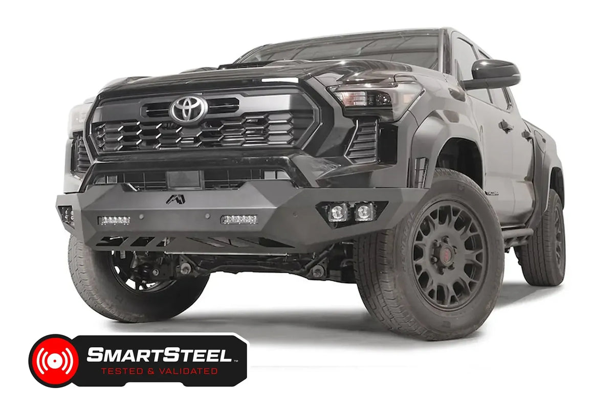 Fab Fours Vengeance front bumper on a dark gray Toyota Tacoma, front three-quarter view, showing the no-guard design, LED light bars, and cube light pods