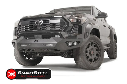 Fab Fours Vengeance front bumper on a dark gray Toyota Tacoma, front three-quarter view, showing the no-guard design, LED light bars, and cube light pods