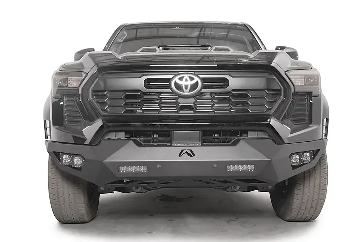 Fab Fours Vengeance front bumper on a dark gray Toyota Tacoma, straight-on front view, showing the full-width bumper, LED light bars, and cube light pods