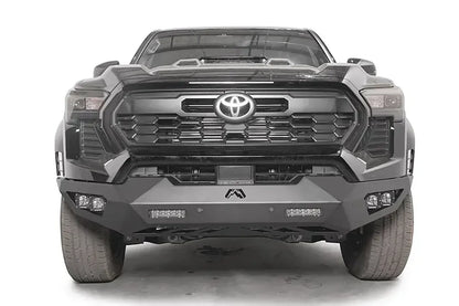 Fab Fours Vengeance front bumper on a dark gray Toyota Tacoma, straight-on front view, showing the full-width bumper, LED light bars, and cube light pods