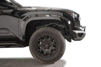 Fab Fours Vengeance front bumper with pre-runner guard on a black Toyota Tacoma, close-up side profile of the front corner, showing the bumper end cap, guard tubing, and wheel clearance