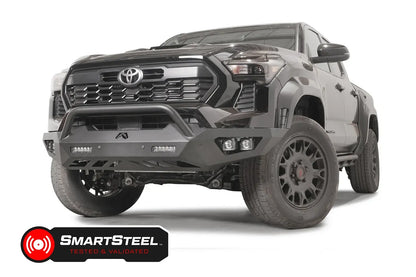 Fab Fours Vengeance front bumper with pre-runner guard on a dark gray Toyota Tacoma, front three-quarter view, showing the pre-runner hoop, LED light bars, and cube light pods