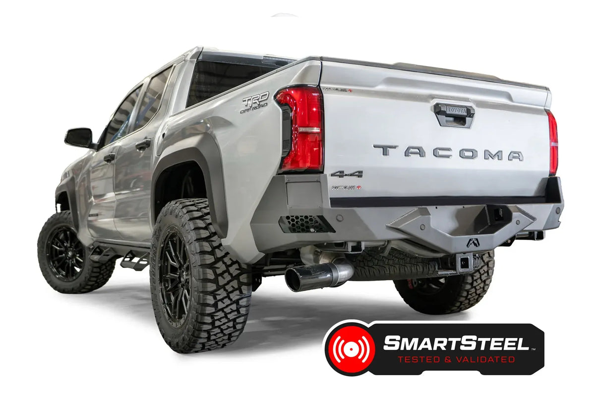 Fab Fours Vengeance rear bumper on a silver Toyota Tacoma, rear three-quarter view, showing the angular end cap, light pod, and center hitch area