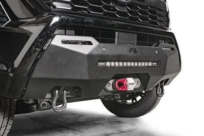 Fab Fours Hidden Winch Mount on a black Toyota Tacoma, close-up three-quarter view, showing the winch fairlead with red hook, LED light bar, and D-ring shackles