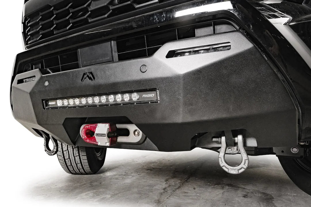 Fab Fours Hidden Winch Mount on a black Toyota Tacoma, close-up front view, showing the winch hook, LED light bar, and D-ring shackle