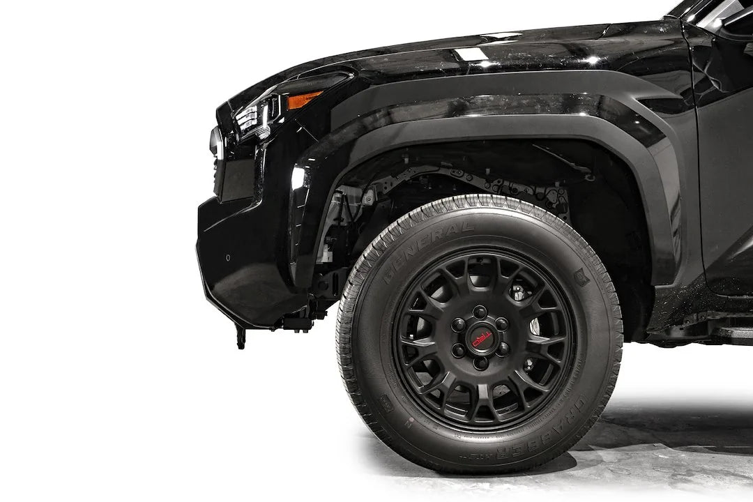 Fab Fours Hidden Winch Mount on a black Toyota Tacoma, close-up side profile of the front corner, showing the bumper end, factory fender fit, and wheel clearance