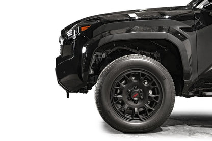 Fab Fours Hidden Winch Mount on a black Toyota Tacoma, close-up side profile of the front corner, showing the bumper end, factory fender fit, and wheel clearance