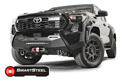 Fab Fours Hidden Winch Mount on a black Toyota Tacoma, front three-quarter view, showing the winch with red hook, LED light bar, and D-ring shackles