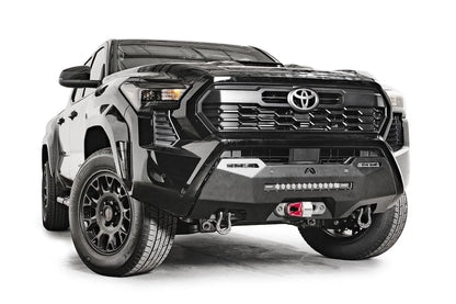 Fab Fours Hidden Winch Mount on a black Toyota Tacoma, front three-quarter view, showing the hidden winch with red hook, LED light bar, and D-ring shackles