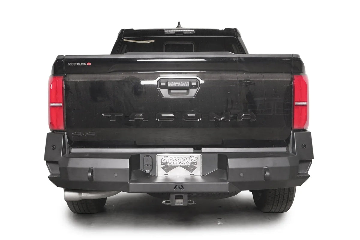 Fab Fours Premium rear sensor bumper on a dark gray Toyota Tacoma, straight-on rear view, showing the full bumper width, sensor-ready face, and receiver hitch