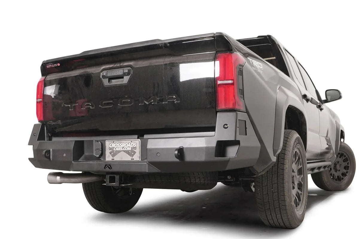 Fab Fours Premium rear sensor bumper on a dark gray Toyota Tacoma, rear three-quarter view, showing the sensor-ready face, recessed lights, and angled end caps