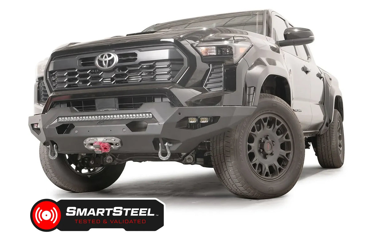 Fab Fours Matrix front bumper on a dark gray Toyota Tacoma, front three-quarter view, showing the LED light bar, cube light pods, and winch fairlead