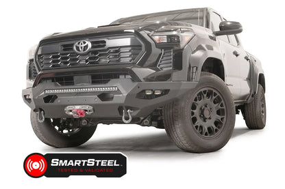 Fab Fours Matrix front bumper on a dark gray Toyota Tacoma, front three-quarter view, showing the LED light bar, cube light pods, and winch fairlead