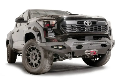Fab Fours Matrix front bumper on a dark gray Toyota Tacoma, front three-quarter view, showing the no-guard design, LED light bar, and winch with red hook
