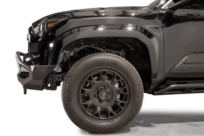 Fab Fours Matrix front bumper with pre-runner guard on a black Toyota Tacoma, close-up side profile of the front corner, showing the bumper end cap, guard tubing, and wheel clearance